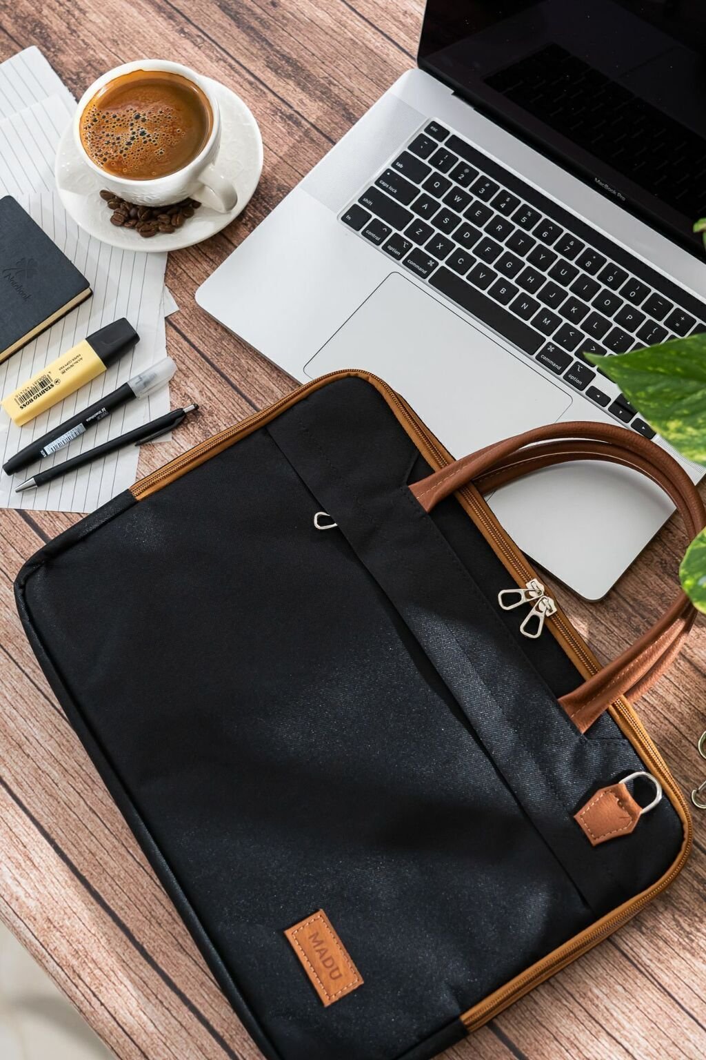 Maletín porta notebook gris de 15.6 pulgadas sobre una mesa con una computadora portátil, una taza de café y útiles de oficina.